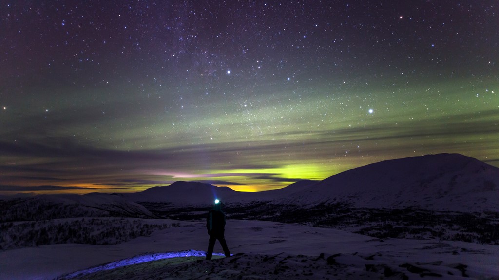 Person på fjäll blickar ut över norrsken och stjärnhimmel